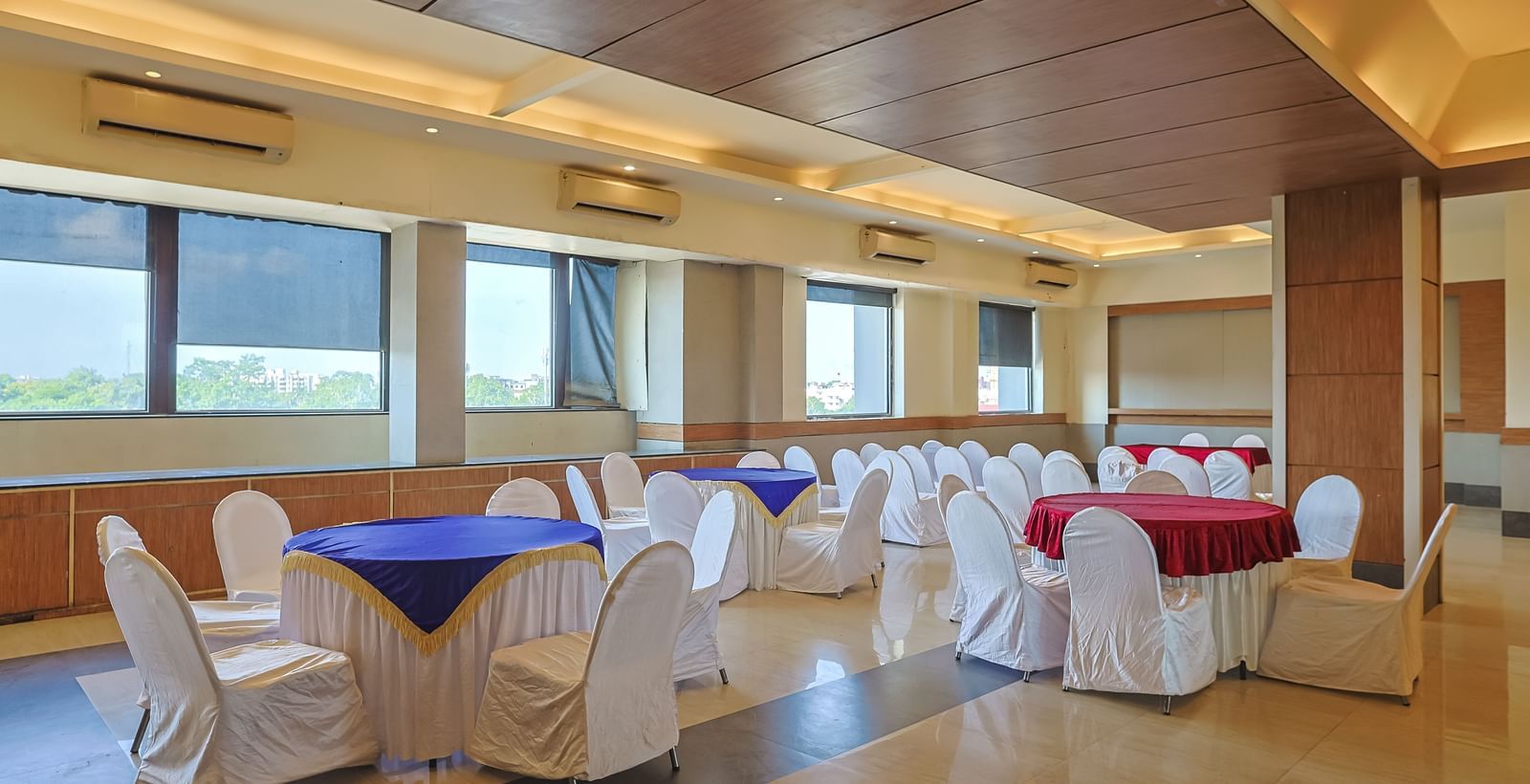 Banquet hall with white chairs, wooden ceiling and bright lighting at Max Hotel Prayagraj.