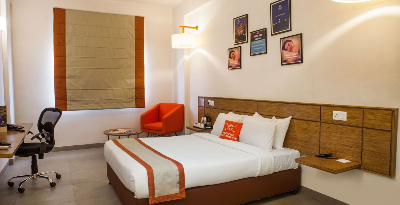 Bedroom with double bed, white sheets, red runner, pillows, desk and wall art at Max Hotel Prayagraj.