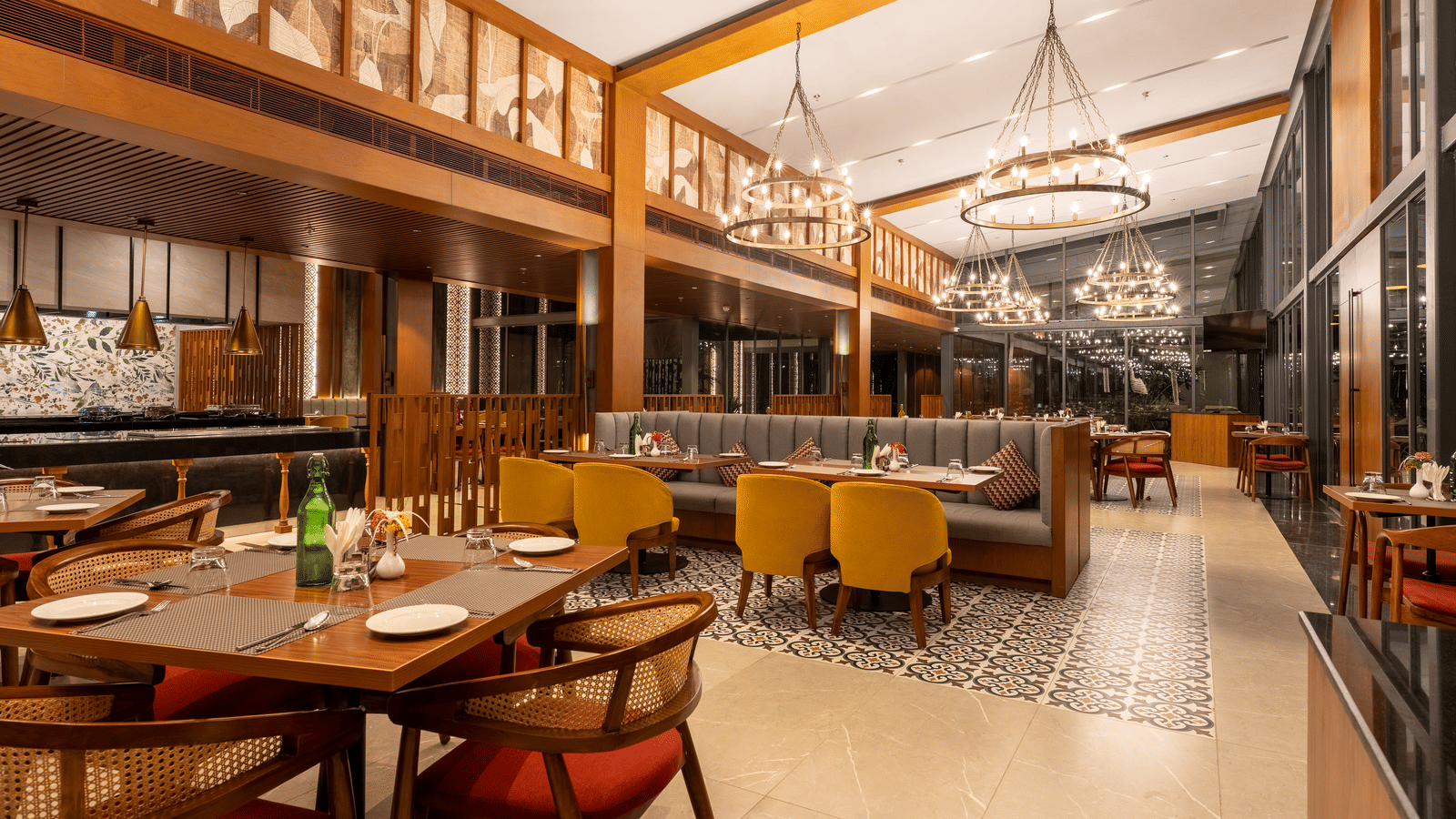 A wide view of the Wyndham Garden restaurant showing multiple dining tables, booths, high wooden beams, and various hanging light fixtures.