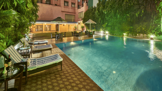An outdoor swimming pool at night with lounge chairs on a tiled deck and trees in the background | HHI Varanasi