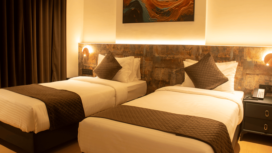 2 single beds room with bedside lamps, headboard panel, and wall art at Magnus Lxia Premier, Kalyani Nagar.