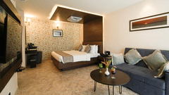 A room with a bed, a sofa with cushions, a table with a flower vase, and a TV mounted on the wall