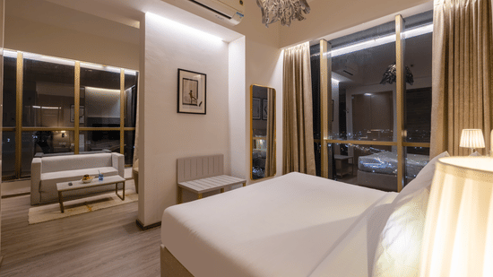 Premium Suite interior at night showing a bed with white linens next to a glass wall partition at Golden Tulip - Sector 80, Gurugram.