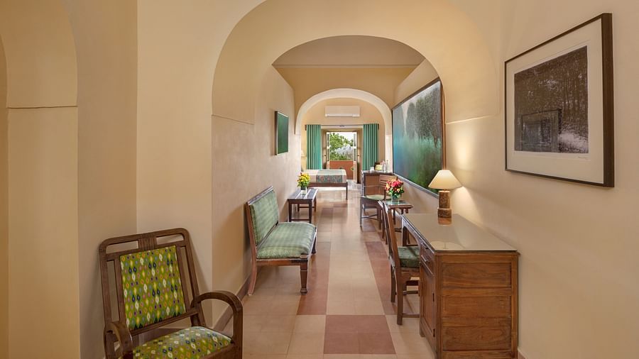 A hallway with an arched doorway leading to a room with a sofa, chairs, and a desk in Tijara Fort-Palace - 19th Century, Alwar.