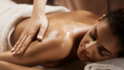A person lying on a folded towel with their eyes closed and receiving a massage on the back of their arms