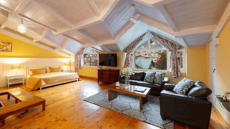 A wide-angle view of a luxury loft living area with leather sofas, wooden floors, and a vaulted ceiling - Johnson Lodge & Spa, Manali