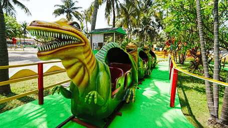 Jurassic Train with a green and yellow dinosaur-head carriage on a track through palm trees, with yellow and red railings at MGM Dizzee World, Chennai.