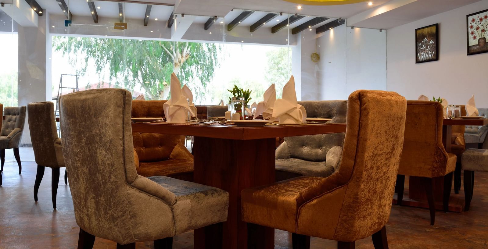 Cosy restaurant interior with plush chairs around a wooden table, set with napkins. - Bamboo Saa, Udaipur