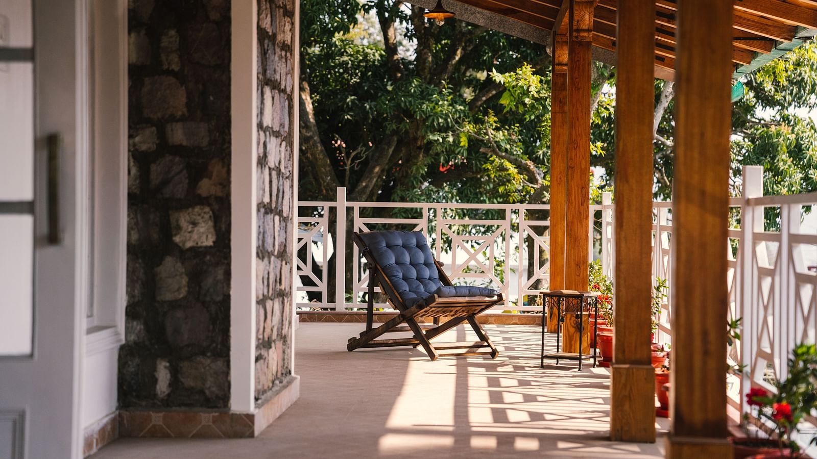 A foldable chair placed on the porch, framed by the stone wall and wooden pillars at BluSalzz Villas - The Green Roof, Bhimtal.