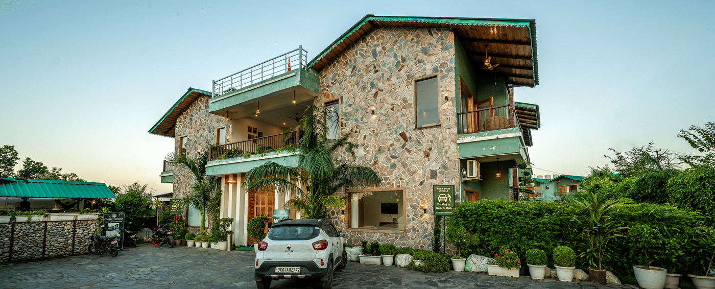 Facade of Corbett Nirvana Resort with cottage-style buildings and a wide lawn