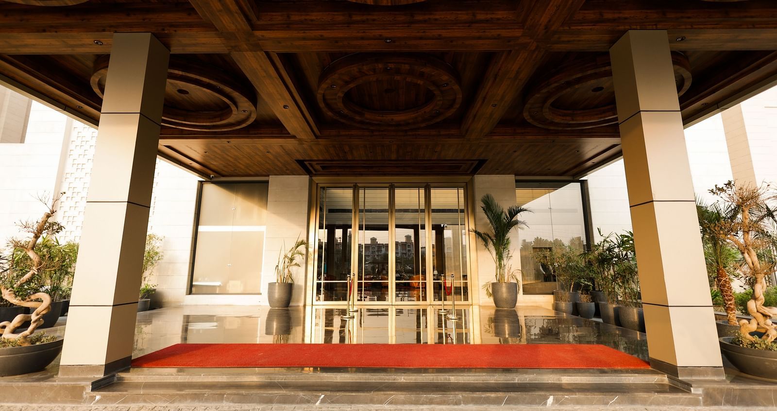 Main glass door entrance with red carpet and potted plants at Ramada by Wyndham Sonipat Murthal
