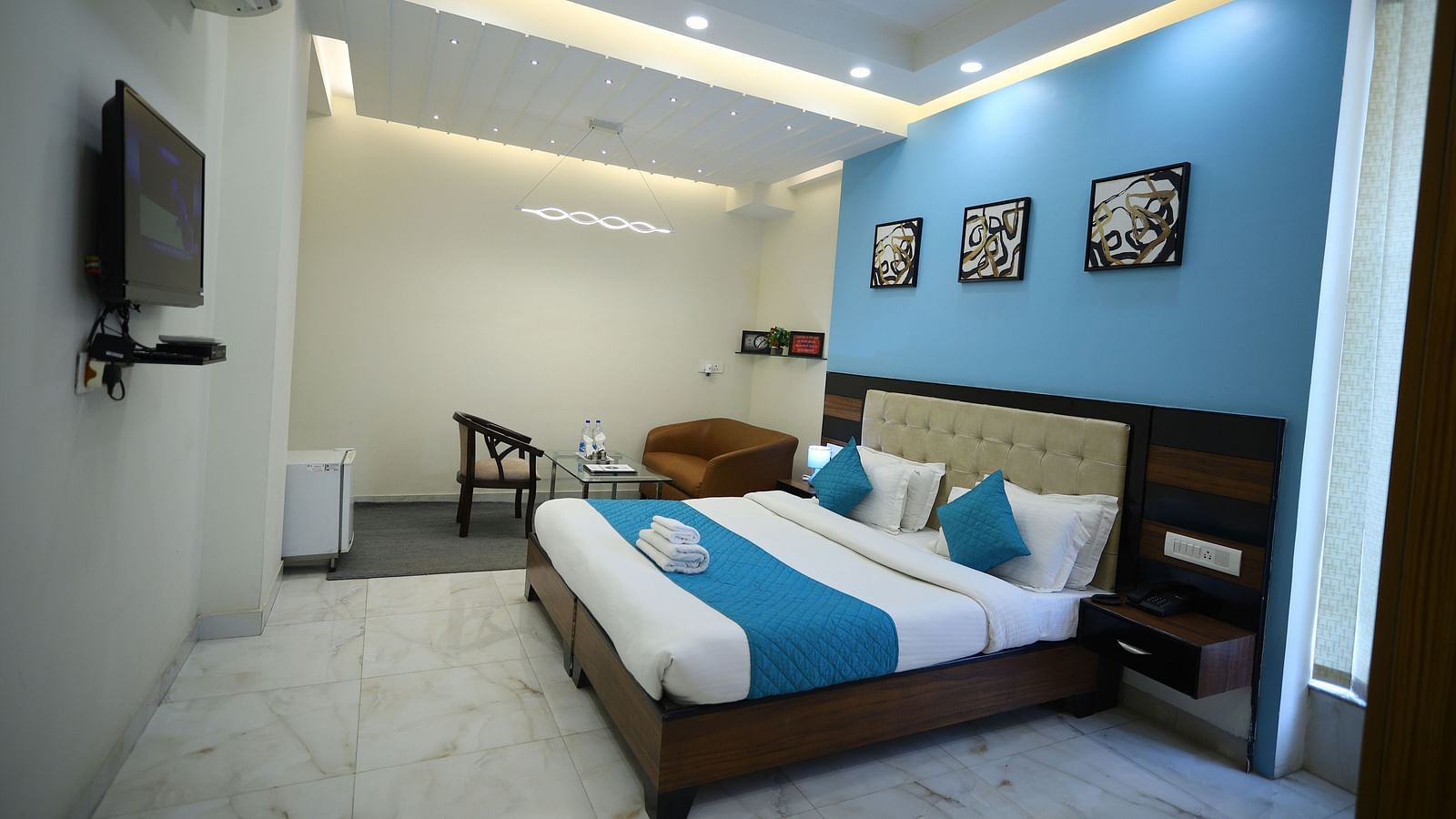 A room with two single beds featuring blue and white bedding, a television, and framed artwork on the wall - Asian Suites Cyber Park, Gurgaon