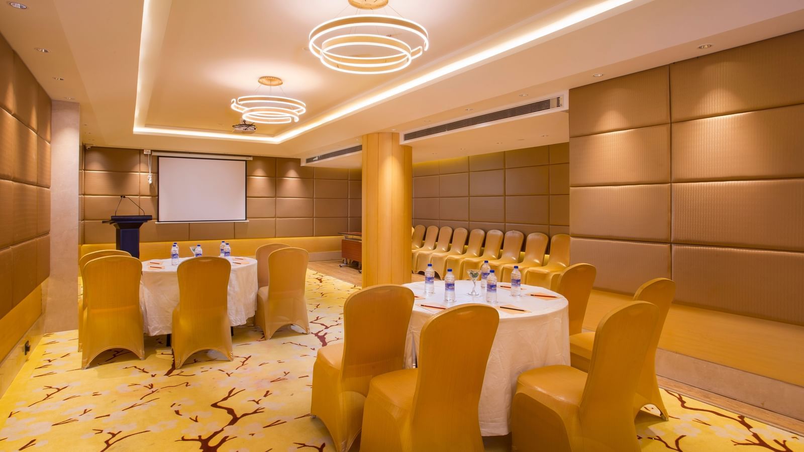 a conference hall with clusters of tables and chairs spread across the hall, where all the chairs are facing the projector - Hotel Fountain Tree By TGI - JP Nagar, Bangalore