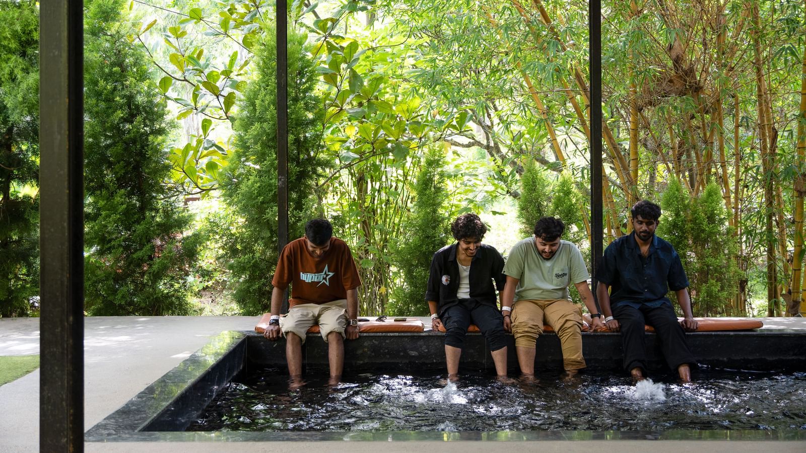 A group of people resting near a pool area with their legs submerged in the water | RD's Nature Retreat, Bangalore