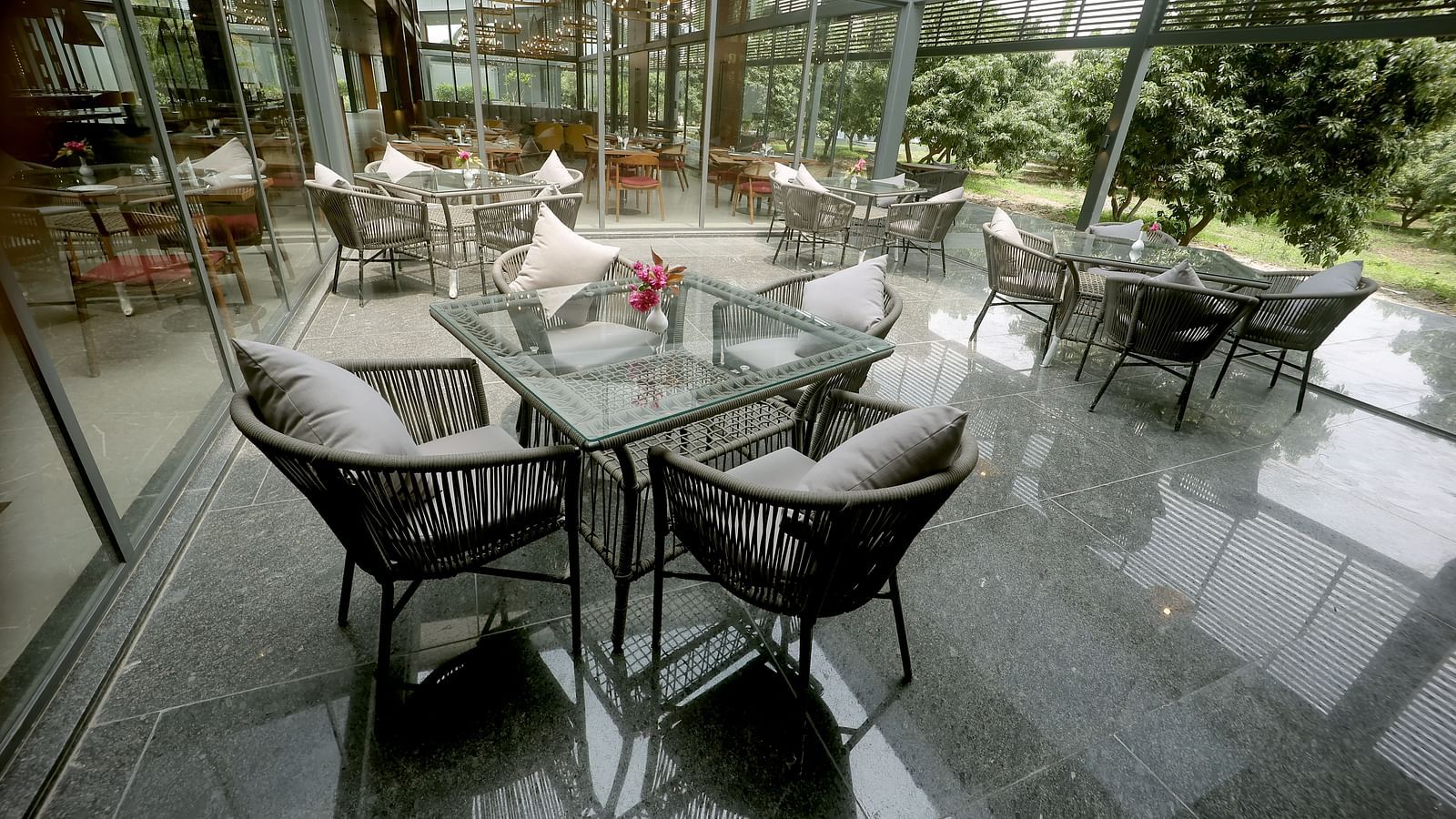 Outdoor dining space with glass walls, grey cushioned chairs, and neatly arranged tables at Wyndham Garden.