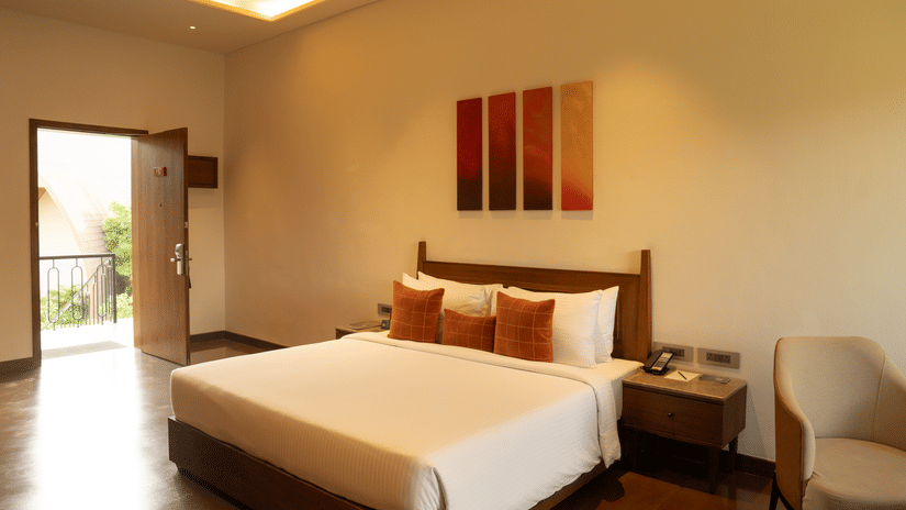 Cosy bedroom with warm lighting, modern artwork, bedside table, a seating area, and outdoor access at Ananta Spa and Resort, Ajabgarh.