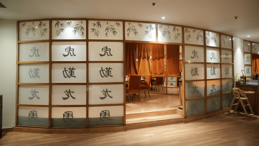 Interior view of an Asian themed restaurant at Park Plaza Ludhiana featuring decorative glass panels with calligraphy wooden flooring curved partition walls and warm ambient lighting.