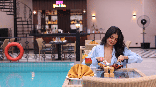 A woman feasting on food at her table next to the swimming pool at Skygrill restaurant with the bar counter in the background