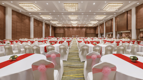 A large banquet hall set up with numerous round tables, white tablecloths, and red runners at Royal Tulip, Kathmandu.