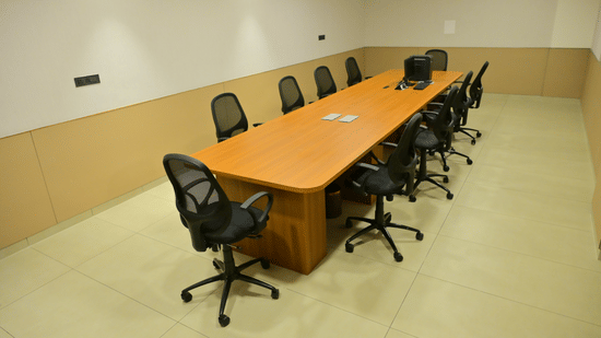Conference room at Bhavanis Vista By Icon Hosur with a long wooden table, black mesh chairs, and warm-toned walls.