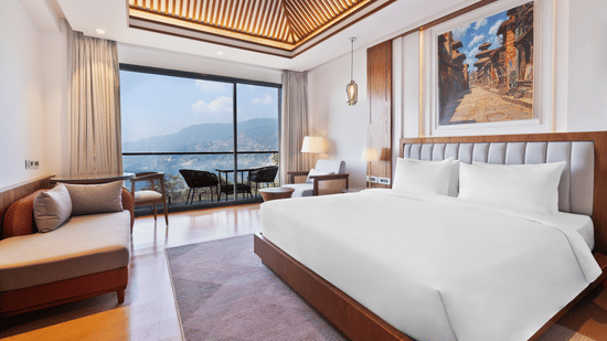 Premium Room bedroom at Royal Tulip Shivapuri National Park - Kathmandu featuring a king bed, a sofa, and a balcony with a view of the mountains.