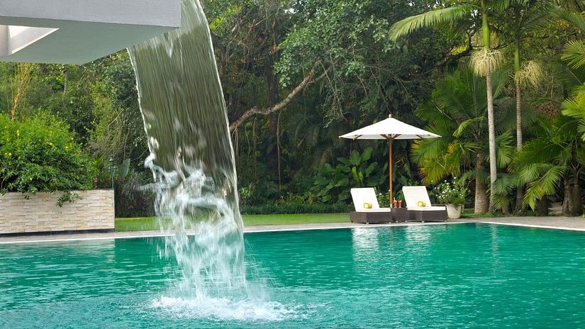 Swimming pool with a waterfall feature surrounded by lush greenery.