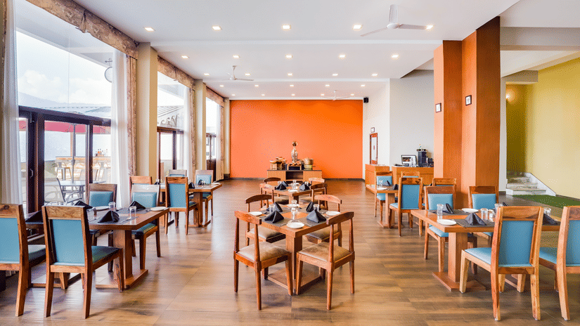 Bright and spacious dining area with wooden furniture and orange accent wall at Mount Himalayan Hotel & Spa, Gangtok.