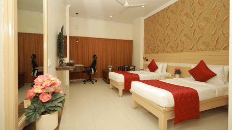An Executive Room at DSF Grand Plaza, Tuticorin with 2 twin beds dressed in red throws, a leaf-patterned feature wall, a wall-mounted TV, and a mirrored wardrobe.