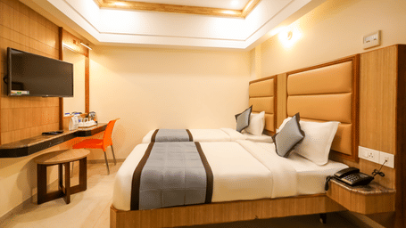 Executive Twin Room with twin beds, wall-mounted Smart TV, desk chair, and ceiling light fixture at Hotel Grand Sabarees Madurai.