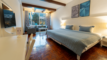 A spacious premium suite featuring light blue bedding, wall-mounted TV, and bright natural light - Johnson Lodge & Spa, Manali