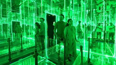 A couple in infinity room at MGM Dizzee World featuring mirrors on all three sides and a pathway on the fourth side, just like how labyrinths are.