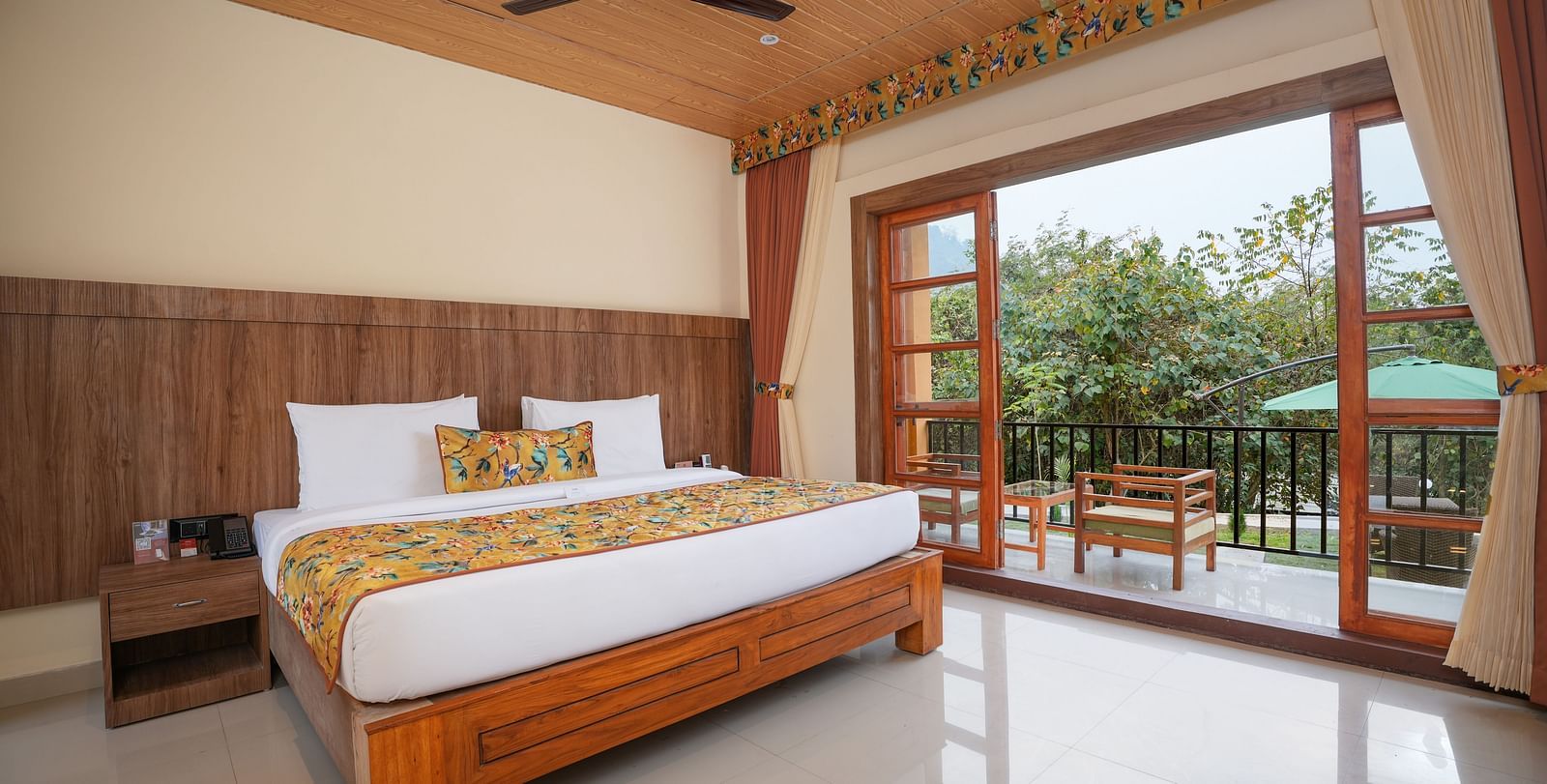 Bungalow featuring a spacious bed with wooden headboards, bedside table, and a large balcony at Summit Green Lake Tea Resort & Spa, Kaziranga