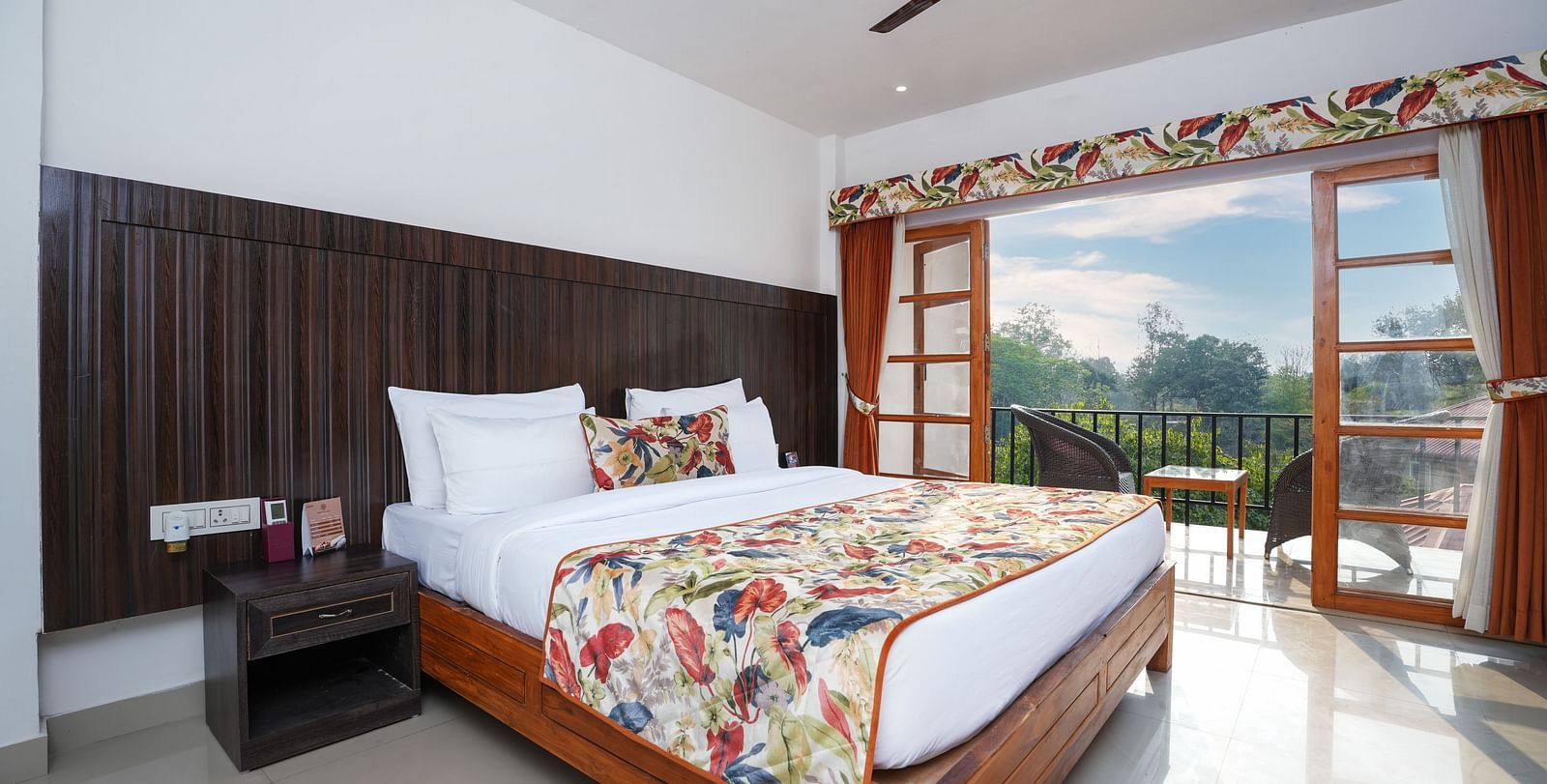 The suite with balcony offers a stunning nature view through large doors that open onto furniture and a glass table at Summit Green Lake Tea Resort & Spa, Kaziranga