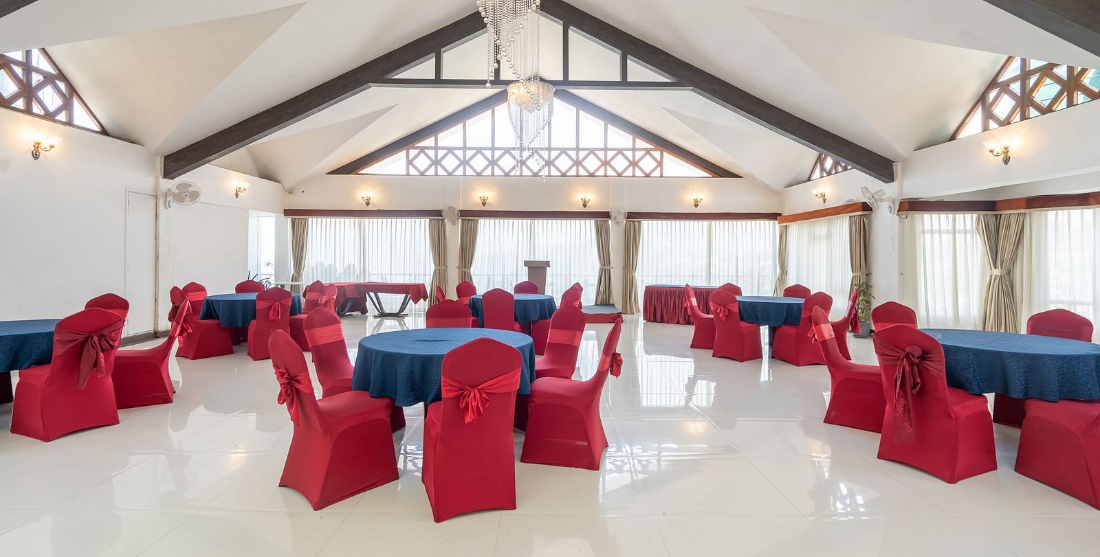 A shot of an expansive banquet hall with a seating arrangement featuring red and blue chairs and tables.