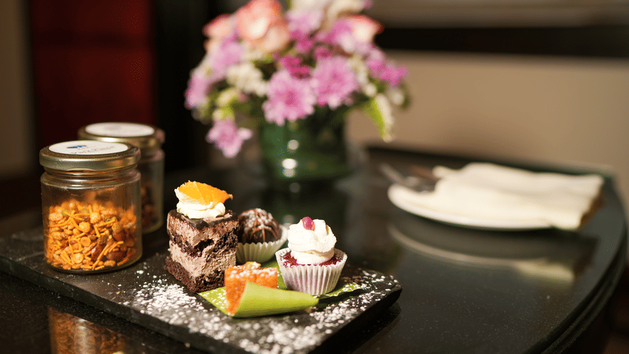 A table setup at Park Plaza Ludhiana featuring snack jars desserts pink flowers in a vase and folded napkins arranged on a dark surface as welcome amenities.