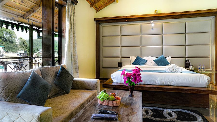 A room featuring a neatly arranged bed, coffee table, sofa, fruit basket, carpet and an adjoining balcony - Vinsober Monal, Nainital     