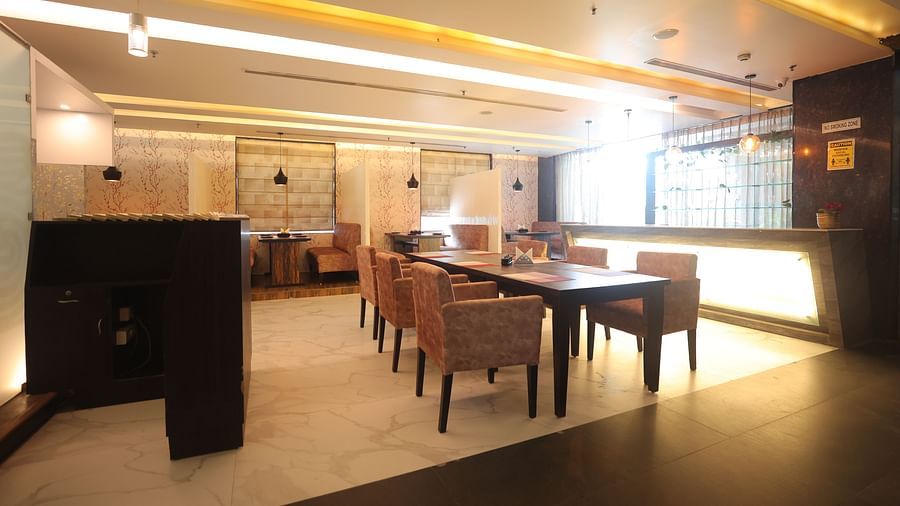 A brightly lit dining area with tables and chairs, soft pink seating, and warm overhead lighting - VITS Gurugram