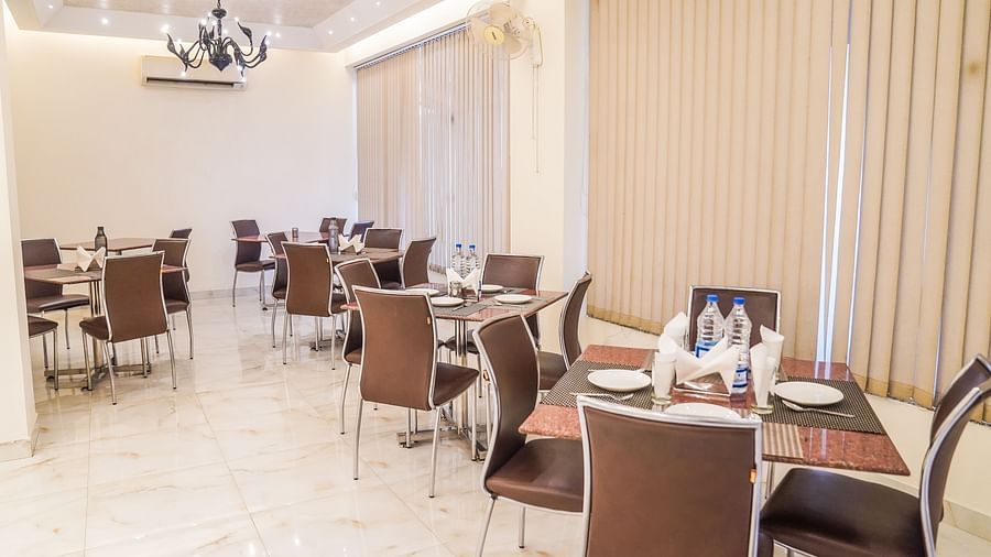 An elegant dining area with multiple tables and chairs is illuminated by a modern chandelier and wall lights - Asian Suites Cyber Park, Gurgaon