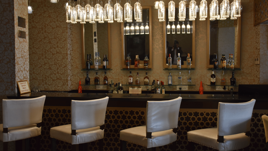 A bar area at Comfort Inn Sapphire by Eastlynn Collections, Jaipur with chairs, counter, shelves, and hanging lights above.