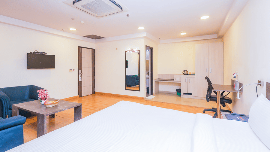 A clean and bright hotel room with a large bed, a small seating area, and essential furniture - Hyphen Business Hotel, Noida