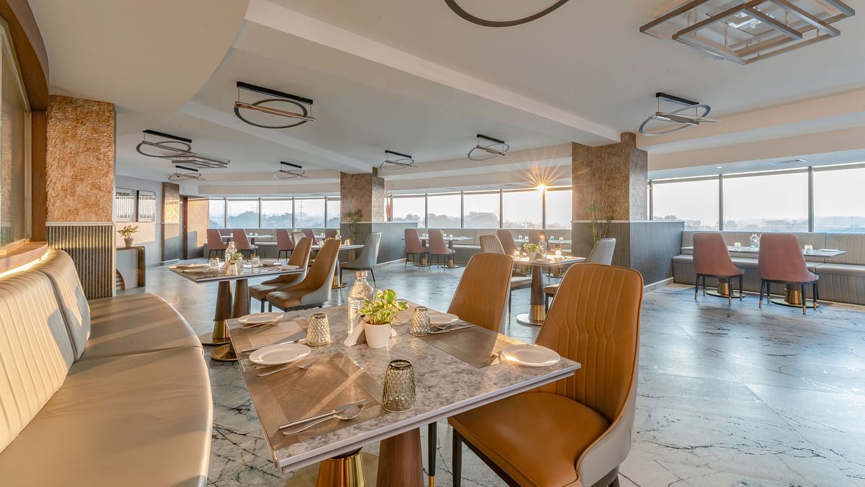 Cosy dining setup with curved banquette seating, marble tables, leather chairs and decorative ceiling lights at Clarks Inn Suites, Hyderabad