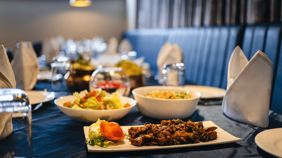 Table set with plates, glasses, napkins, and assorted dishes, including salad and cooked food, in dining area at The Residences at CSE.