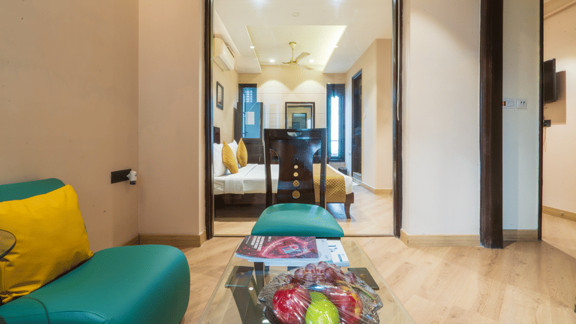 Suite living area at Cosy Grand @Chanakyapuri by The Cosy Hotels with teal sofa seating and connected bedroom.