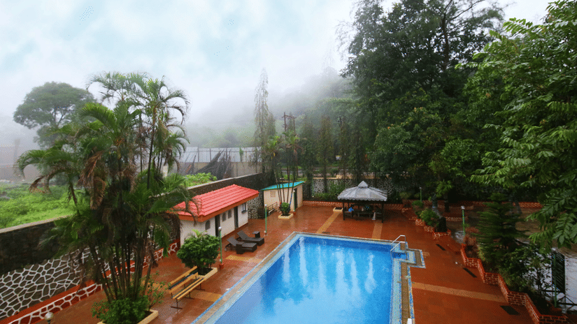 A tranquil swimming pool sits at the heart of a lush garden with mist lingering among the trees | Zara's Resort