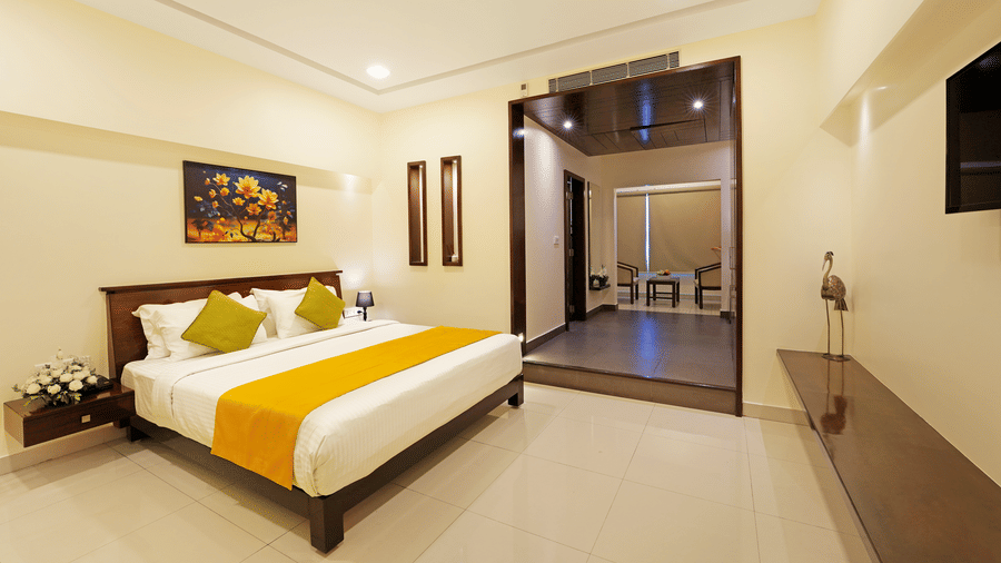 A Premium Room at Clover - A Rivido Hotel, featuring a neatly-made bed, a floral painting above the headboard, a decorative bird showpiece, and a large open doorway.