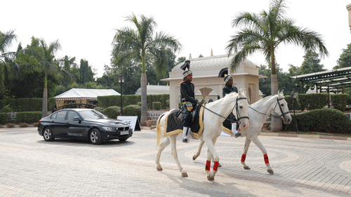 Grand entrance of a luxury hotel with a horse-mounted guard and a vintage car on display.