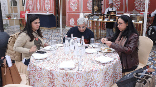 Three people sitting around a round table with bottles, glasses and plates placed on it.- Heritage Village Resorts & Spa