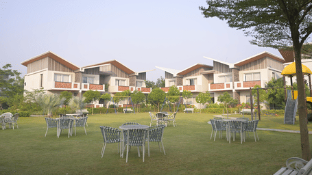 Open green lawn with white outdoor seating and rows of villas in the distance at Hotel Sonar Bangla, Mayapur.