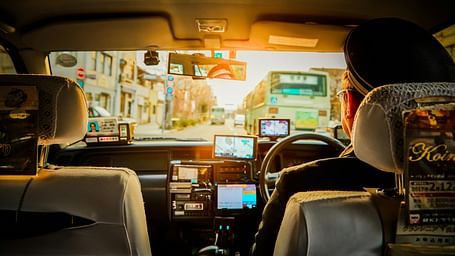 Backseat view of a car showing the driver and front passenger seats with sunlight streaming through the windscreen onto the dashboard and street.