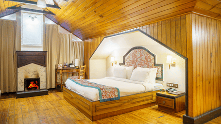A room at Orsino Spa Resort, Darjeeling, with a wooden ceiling, a bed with a patterned throw, and a small fireplace.